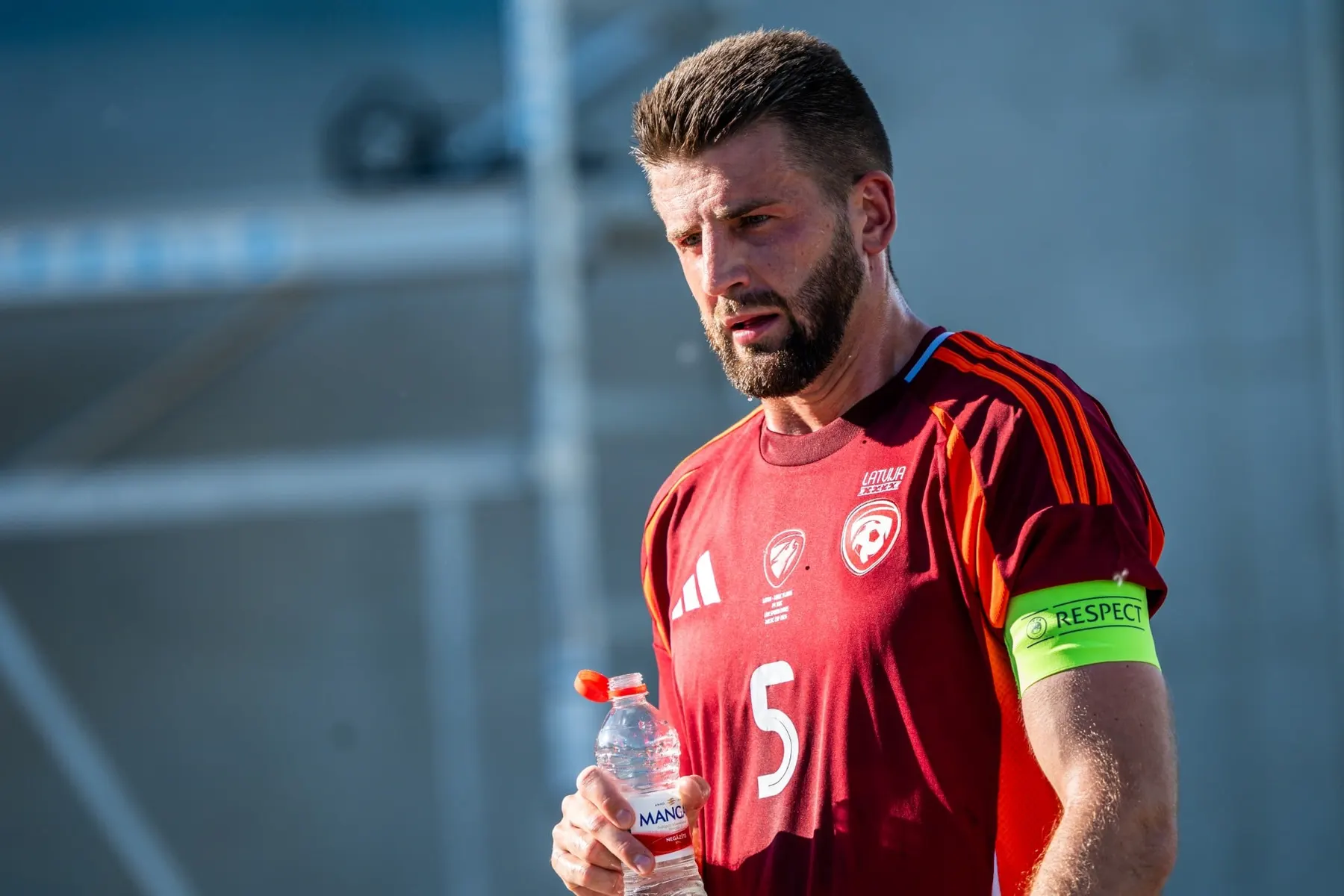 Latvijas izlases futbolists ar kapteiņa apsēju saulainā dienā